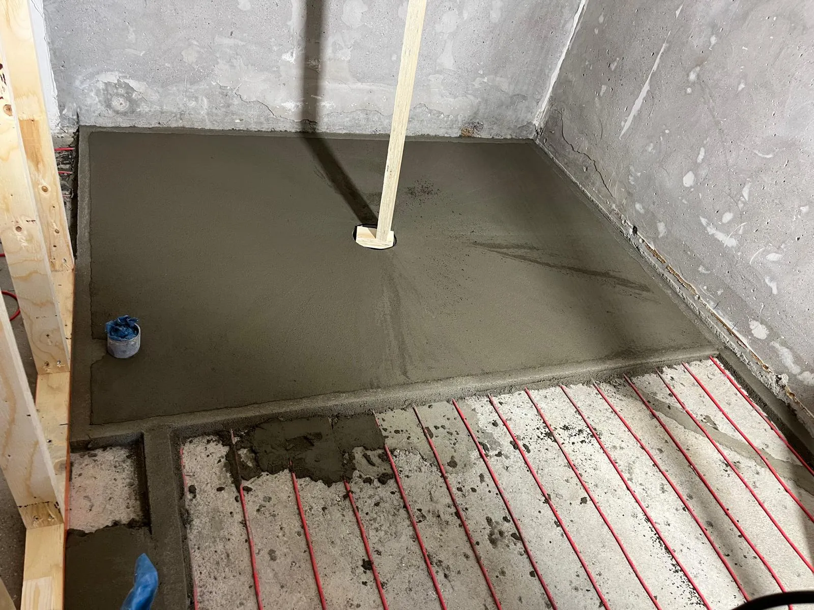 Huoneen lattia on osittain valettu betonilla, jossa on lattialämmitysputket ja puinen tukipalkki.