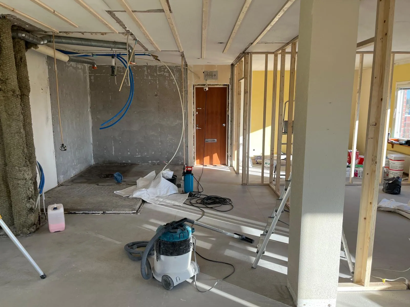 Rakennustyömaa, jossa on tyhjä huone, jossa on paljaat seinät, puinen katto ja keskellä pölynimuri.