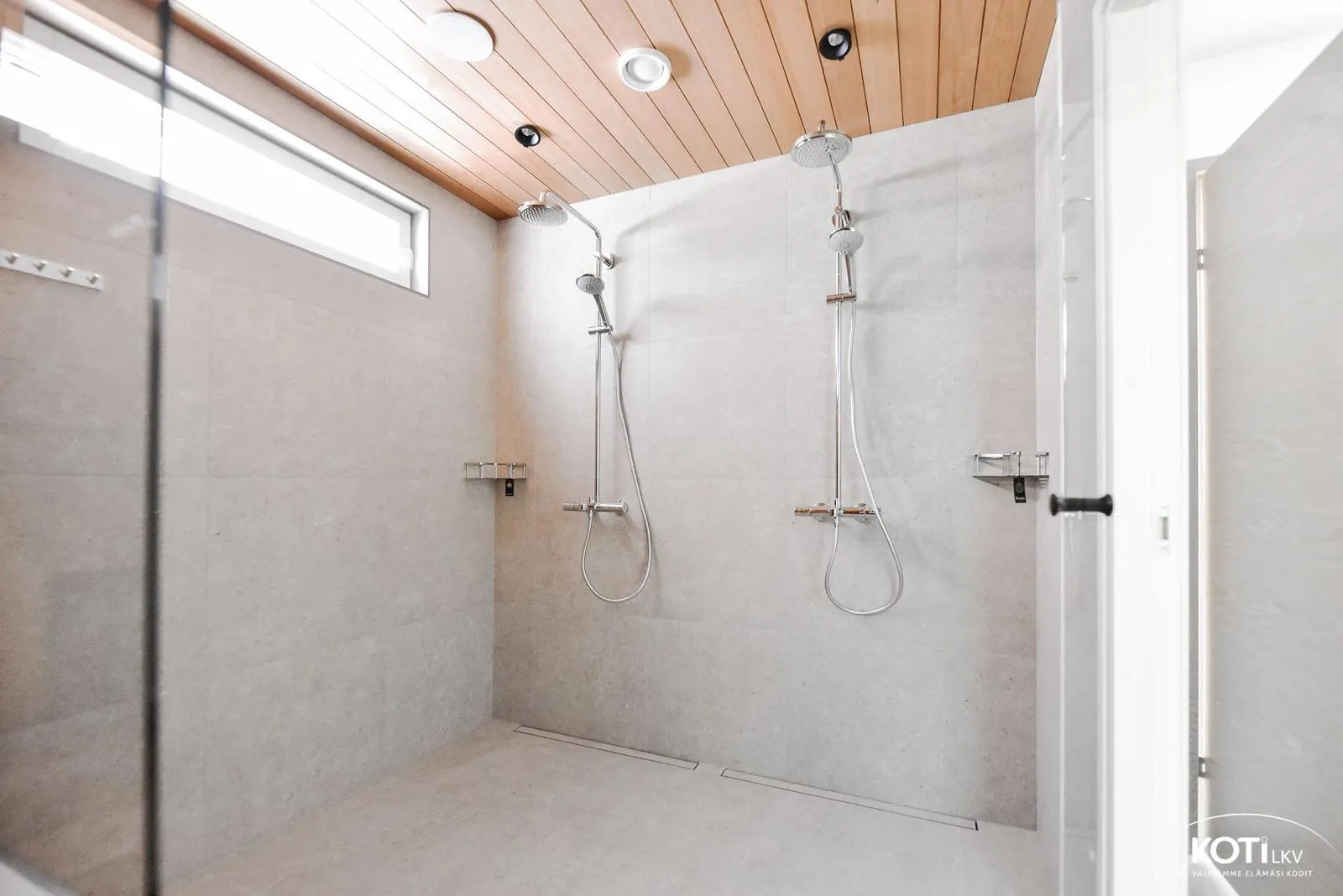 Moderni kylpyhuone, jossa on kaksi suihkua, puinen katto ja harmaat laatat.